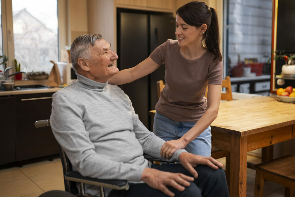 weibliche Pflegekraft betreut einen Senior mit Stoma im Rollstuhl in dessen heimischen Umfeld